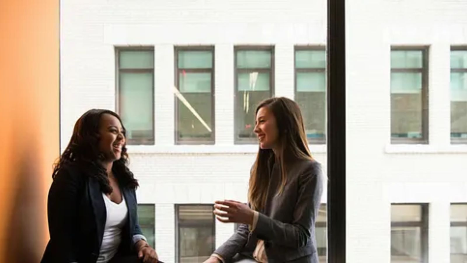 Two women discussing career advice during a coaching conversation, office building in the background